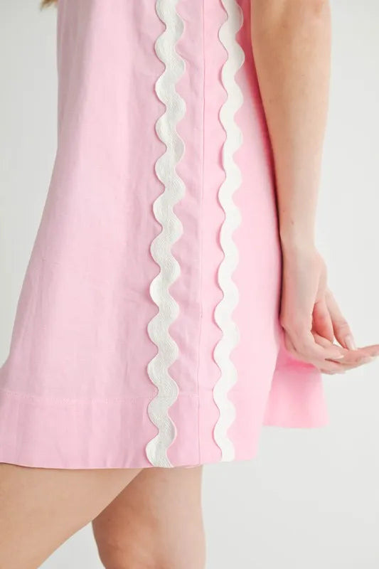 Pink dress with white scalloped trim on a plain background
