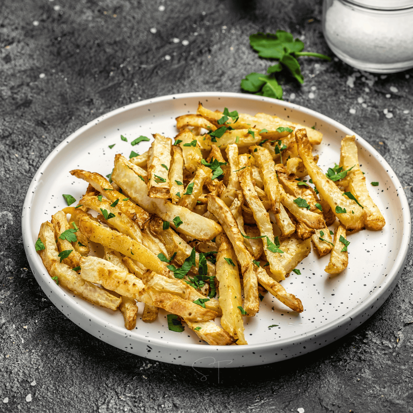 Plate of parsnip fries with herbs on a dark surface
