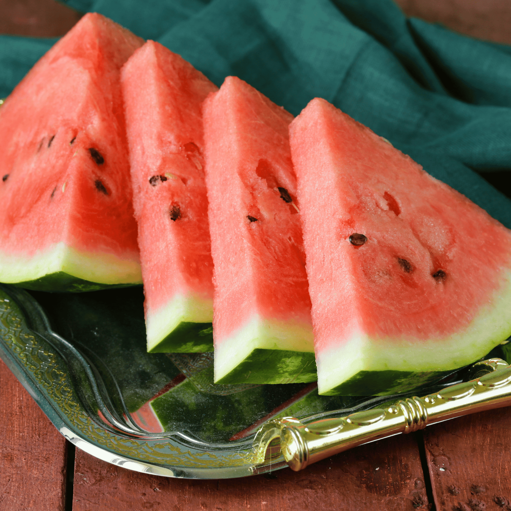 Slices of watermelon on a glass plate with a gold handle, on a wooden surface.