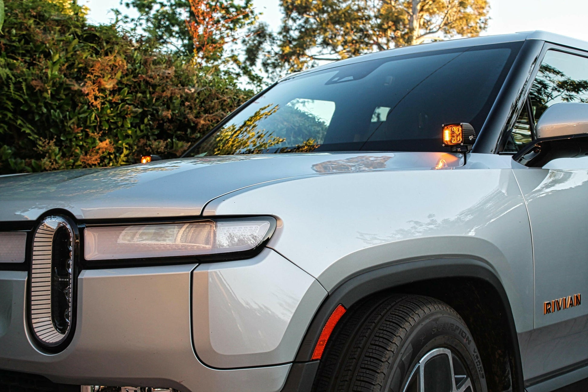Close-up of a silver electric vehicle with 'Rivian' branding, and an amber LED Light bar mounted on drivers side.