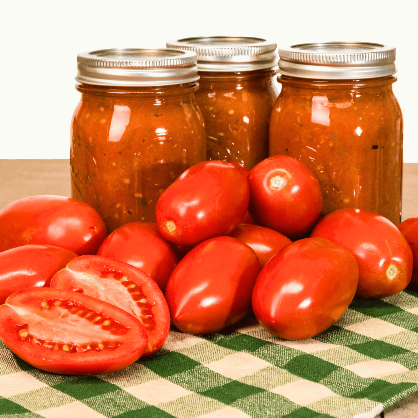 Jars of canned tomatoes and fresh Amish Paste tomatoes on a checkered tablecloth