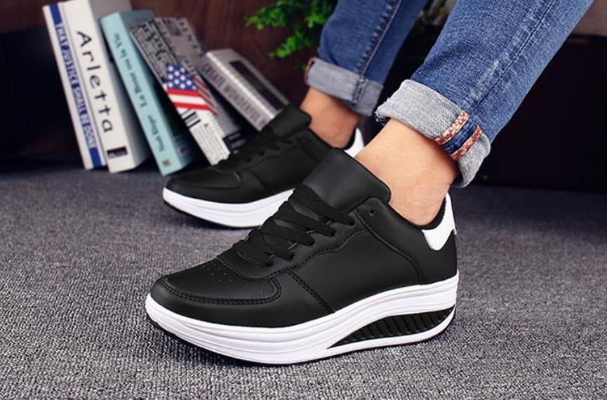 Black sneakers with white soles worn by a person, with books and a plant in the background.