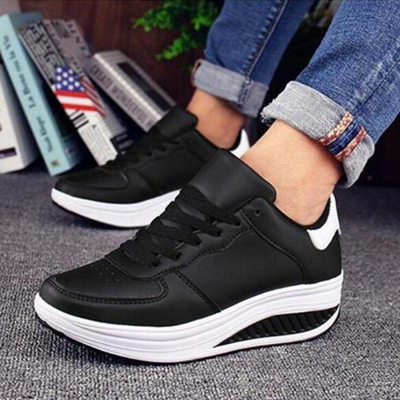 Black sneakers worn with rolled-up jeans on a gray surface.