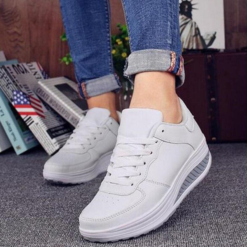 White sneakers worn with rolled-up jeans on a gray floor.
