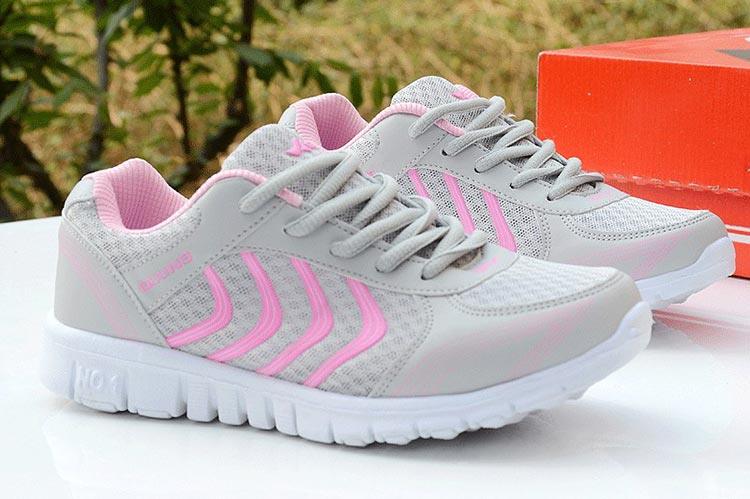Gray running shoes with pink accents on a white surface, with a blurred natural background.