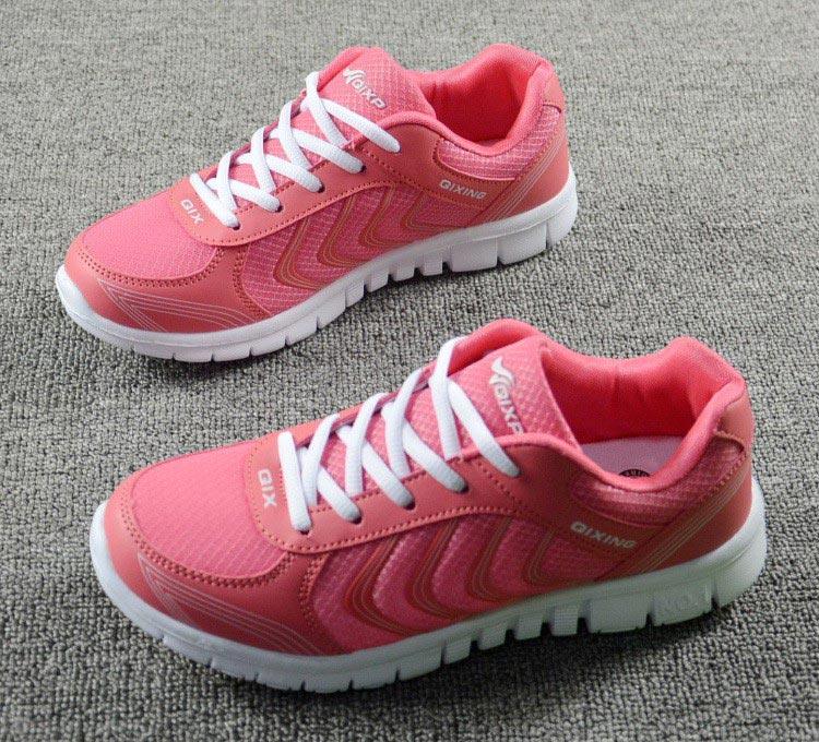 Pair of pink running shoes with white laces on a gray surface