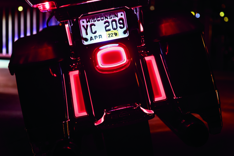Close-up of a motorcycle with illuminated red lights and a visible license plate at night.
