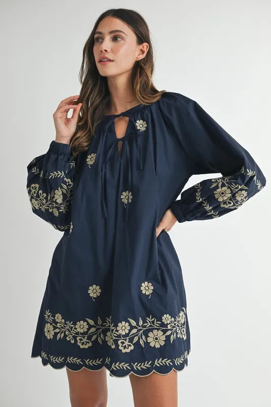Woman wearing a navy dress with floral embroidery on a white background
