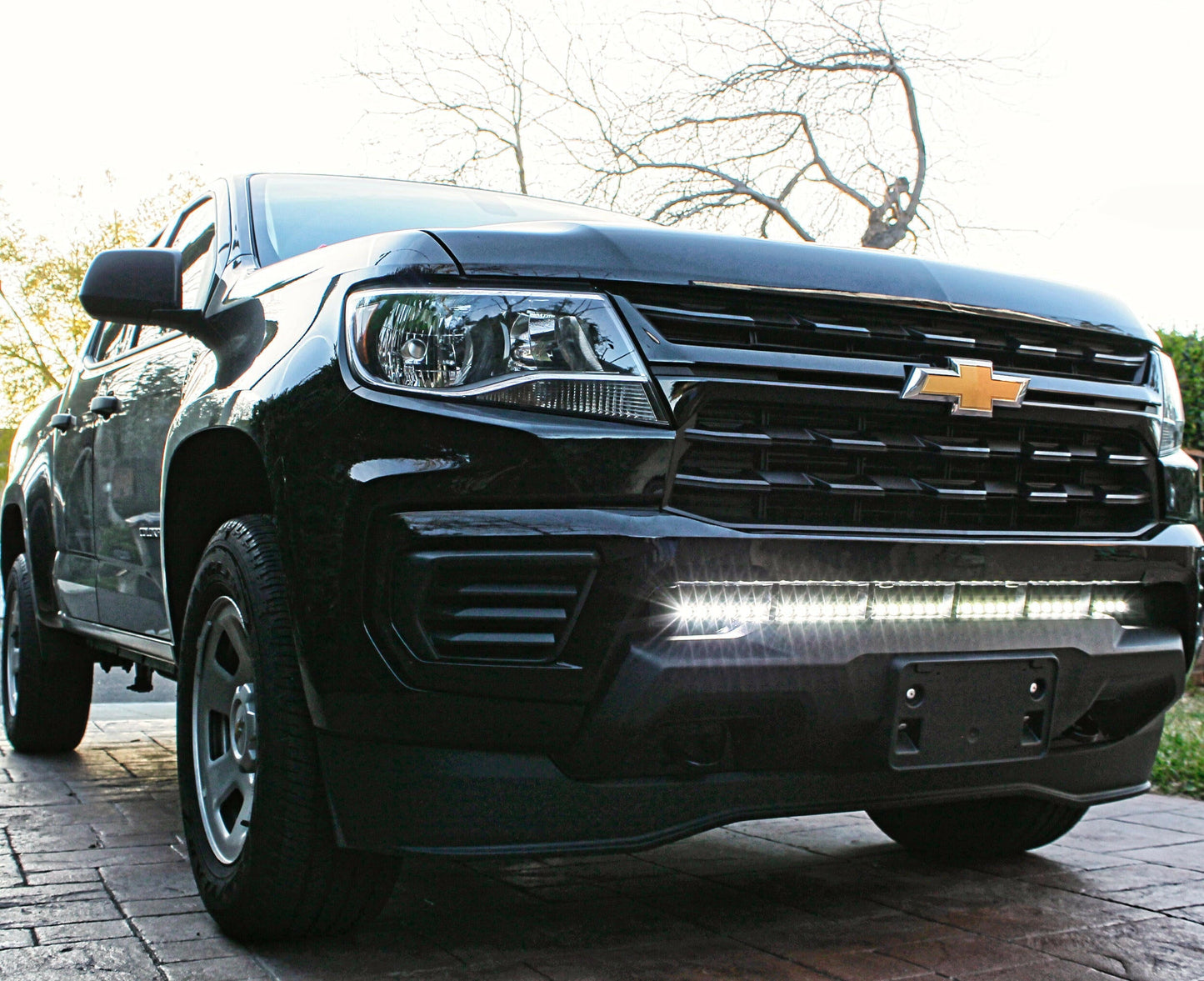 Black Chevrolet truck parked on a brick driveway with trees in the background