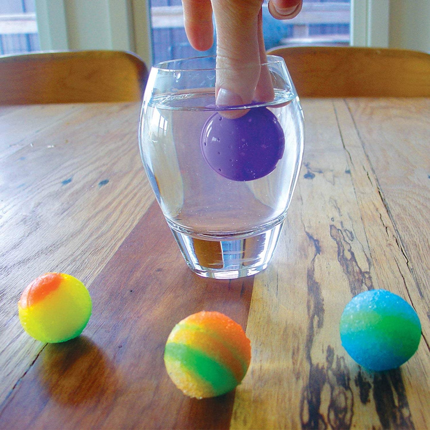 Colorful balls on a wooden table with a glass of water.