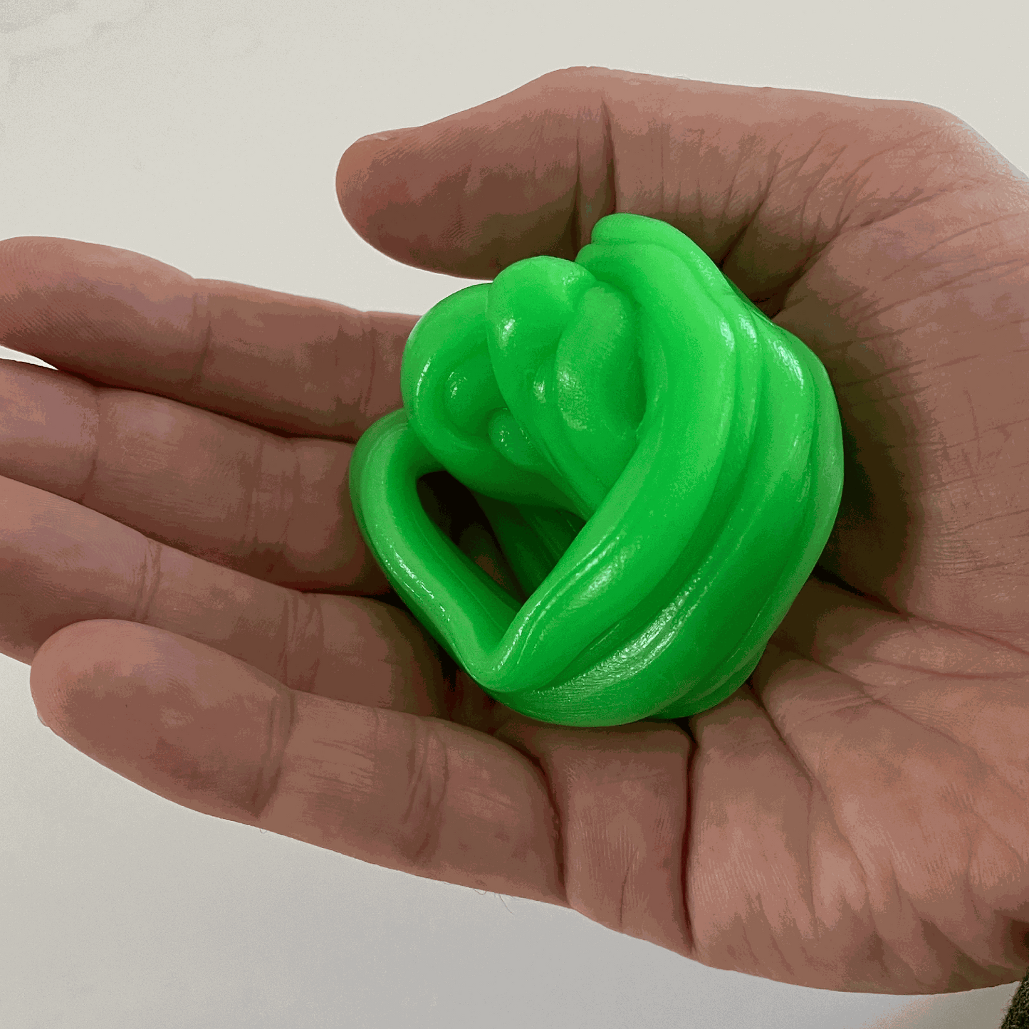 Hand holding green gootonium putty against a plain background