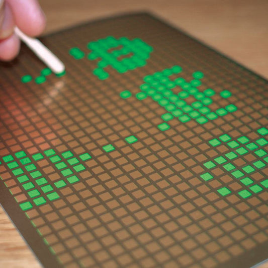Pixelated text on a grid mat with a hand holding a pen.