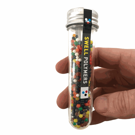 Hand holding a tube of Swell Polymers with colorful beads inside on a white background