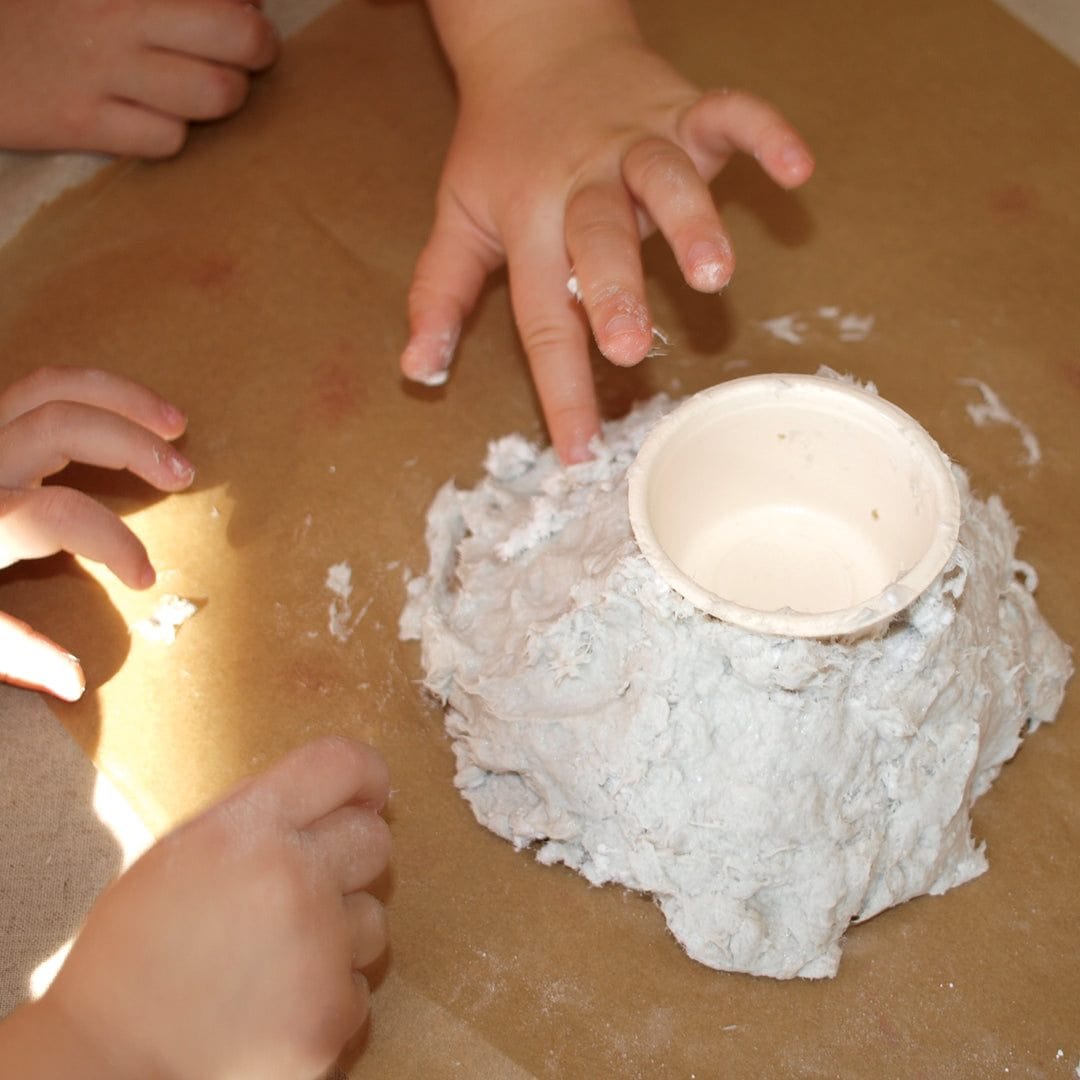 Children's hands working with a clay pot on a brown surface