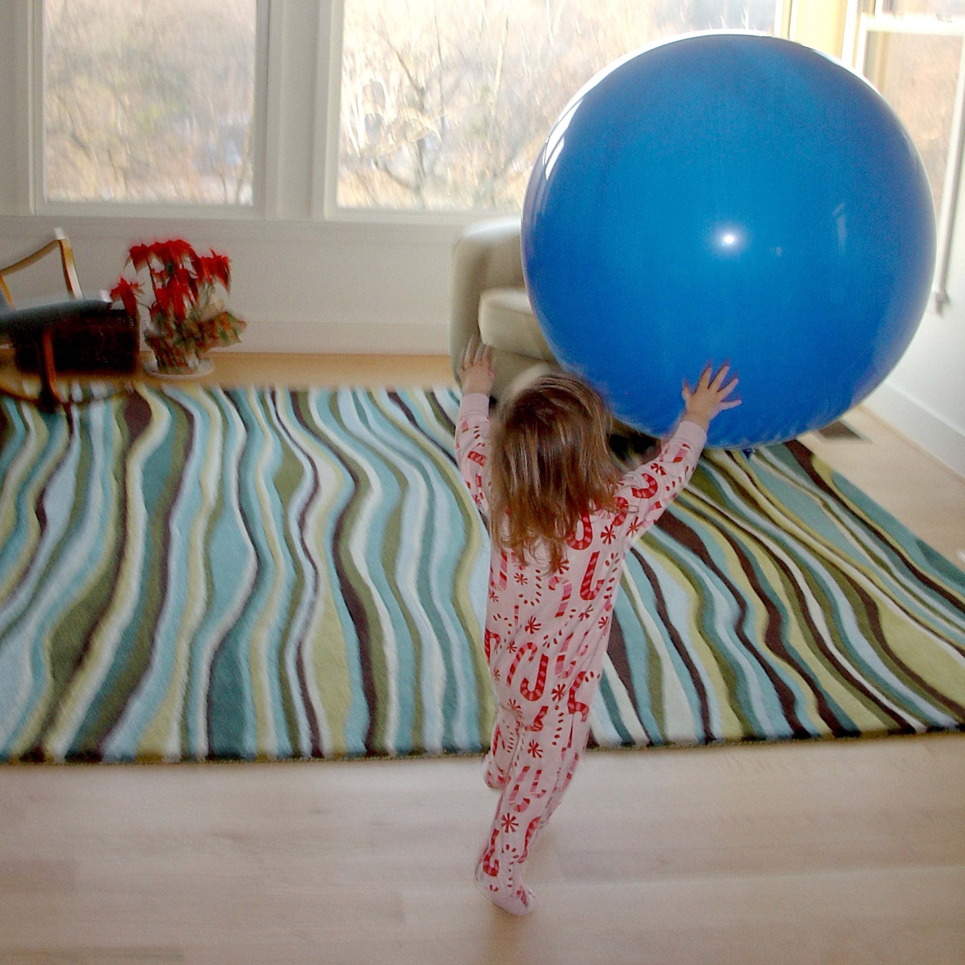 Child playing with a large blue balloon indoors on a patterned rug.