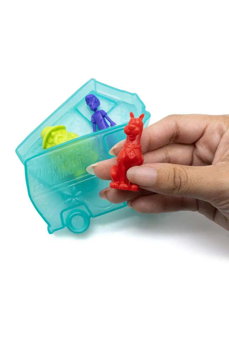Hand holding a red toy scooby doo  figure next to a transparent blue container with colorful figures inside on a white background