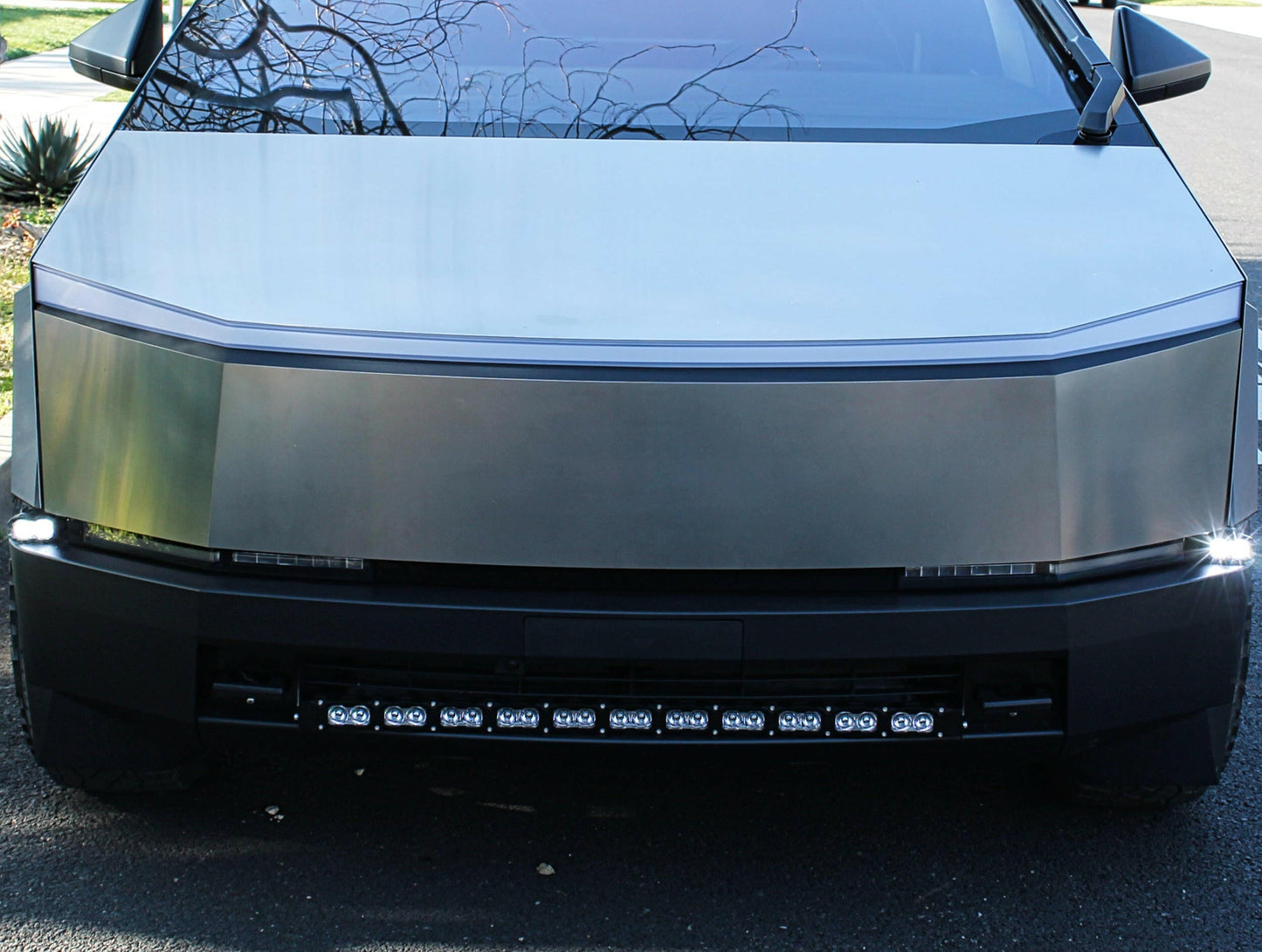 Front view of a tesla car with a reflective hood and led light strip.