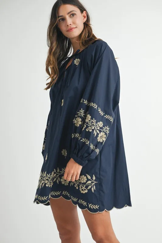 Woman wearing a navy blue dress with floral embroidery on a white background