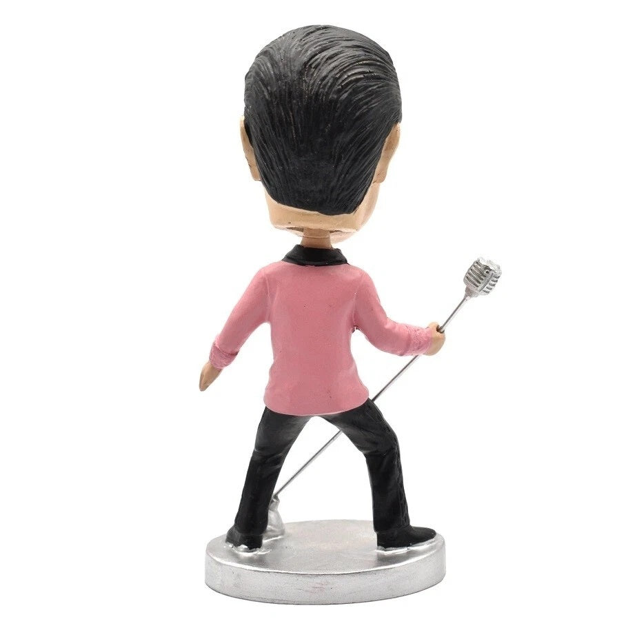 Bobblehead figure of Elvis Presley in a pink shirt and black pants holding a silver object on a white background