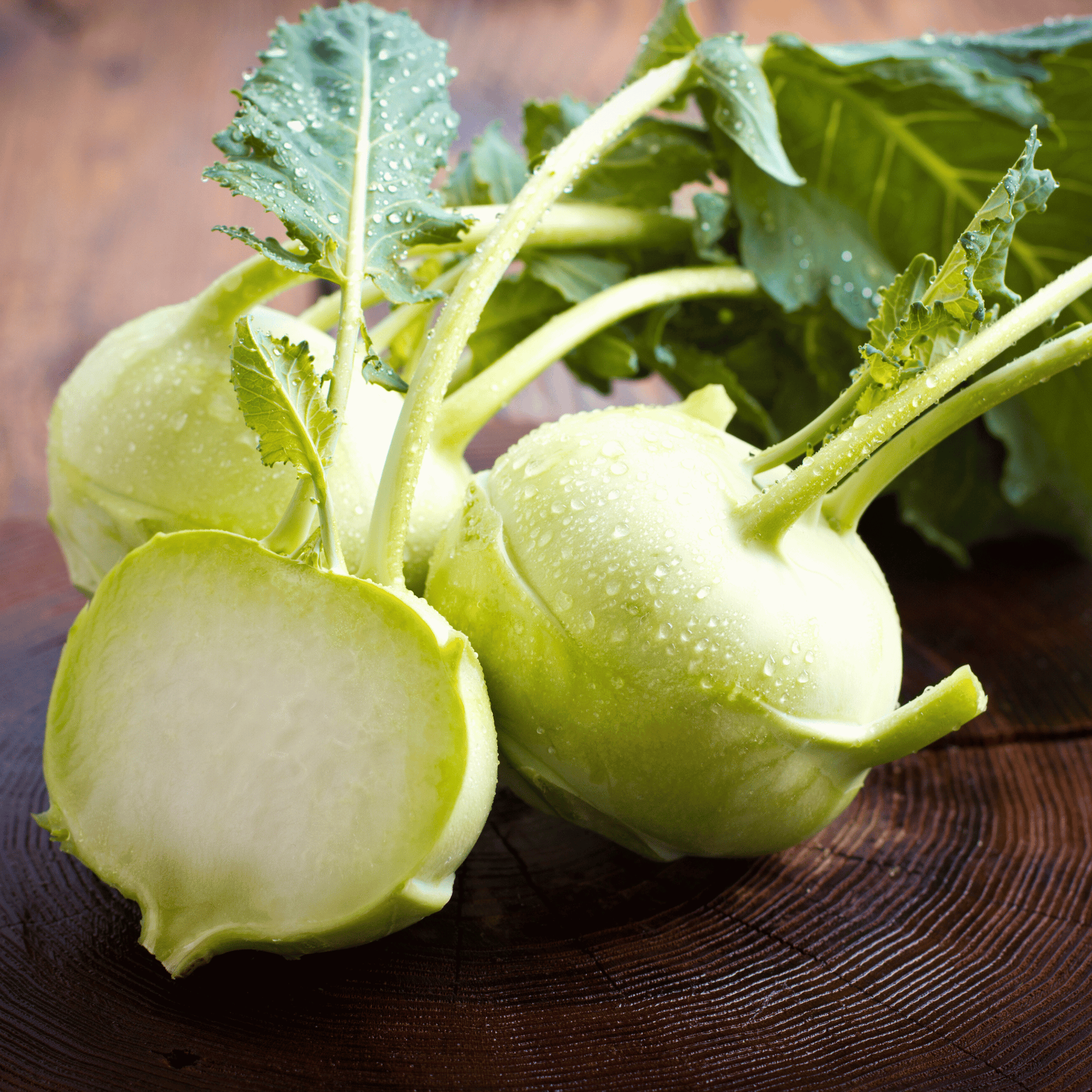 Two green kohlrabi bulbs on a wooden surface