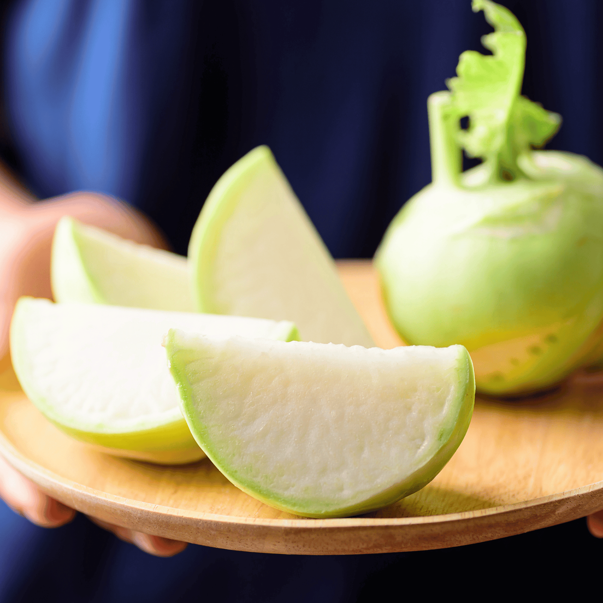 Sliced green kohlrabi on a wooden plate with a whole kohlrabi in the background.