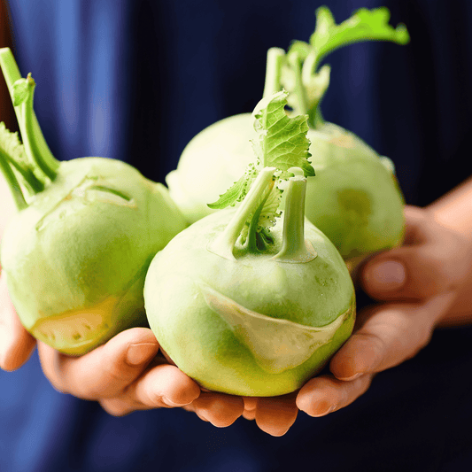 Three green kohlrabi bulbs held in hands against a dark background