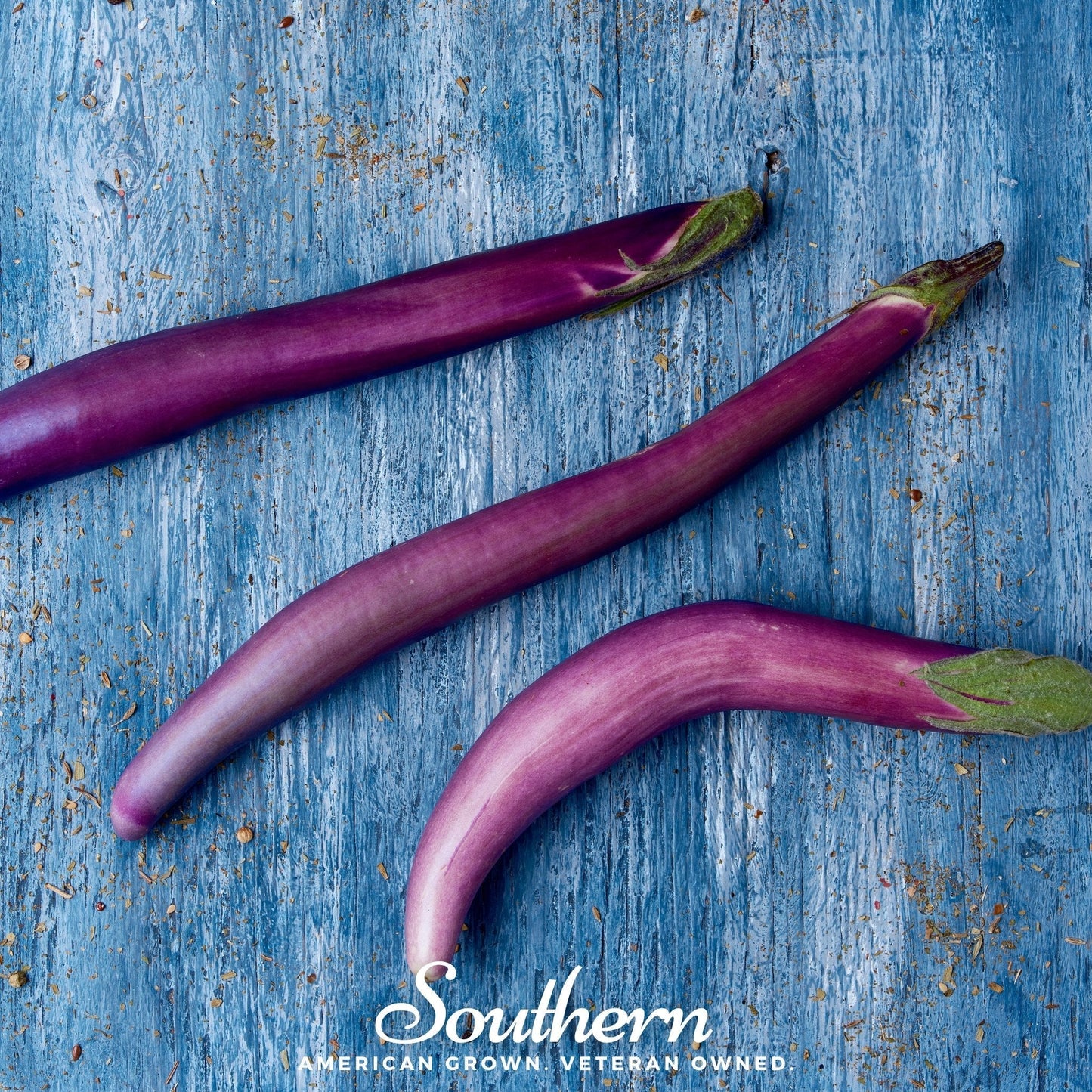 Three purple eggplants on a blue wooden surface with 'Southern' branding.