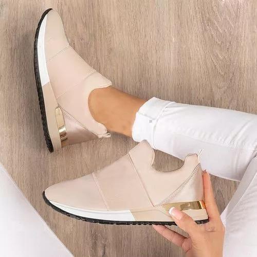 Beige wedge shoes with gold accents being held by a person against a wooden floor background.