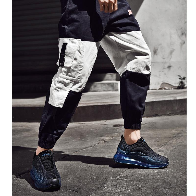 Person wearing black and white pants with blue sneakers on a concrete surface.