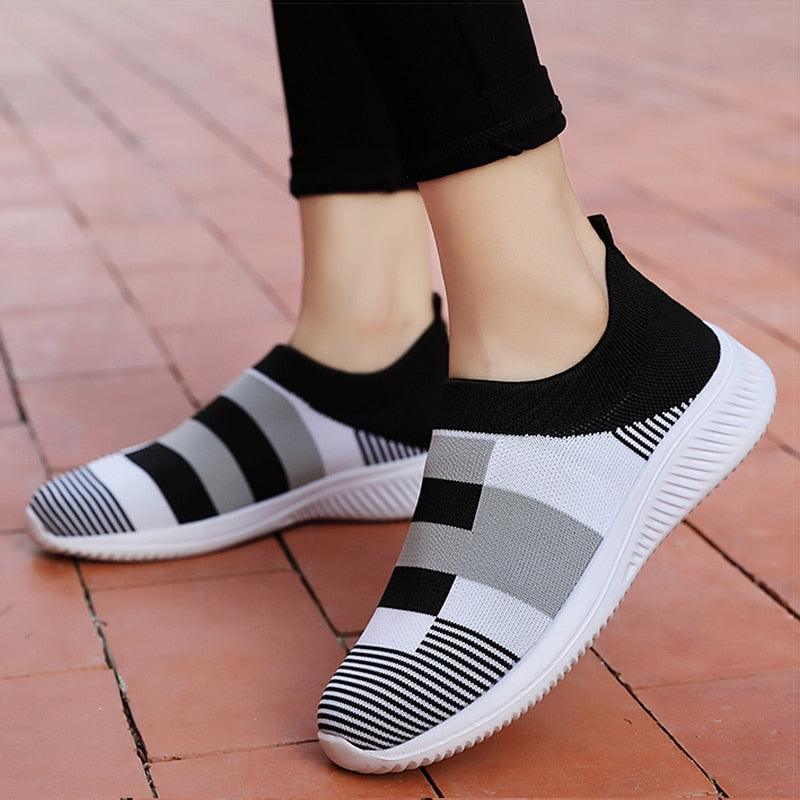Black and white checkered slip-on shoes on a person's feet with a checkered floor background