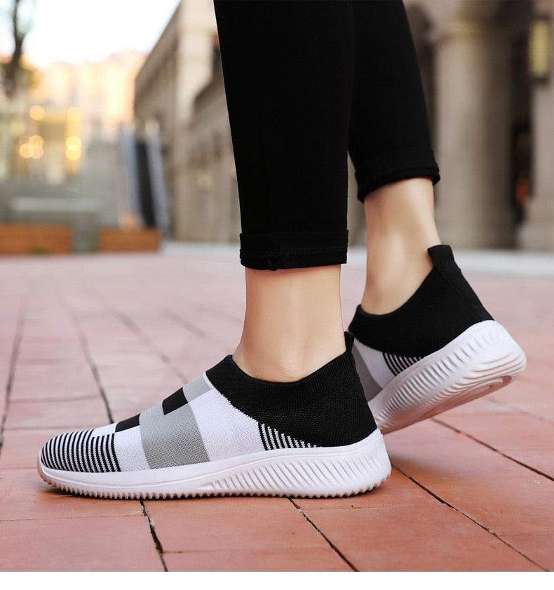 Black and white slip-on sneakers worn on a blurred outdoor background