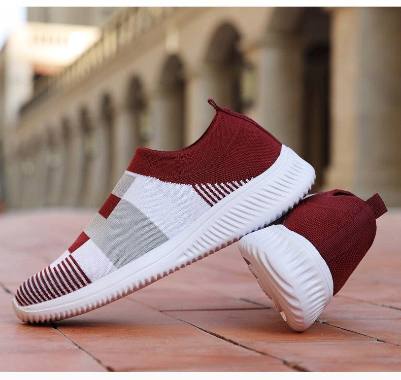 Maroon and white slip-on sneakers on a wooden floor with blurred architectural background