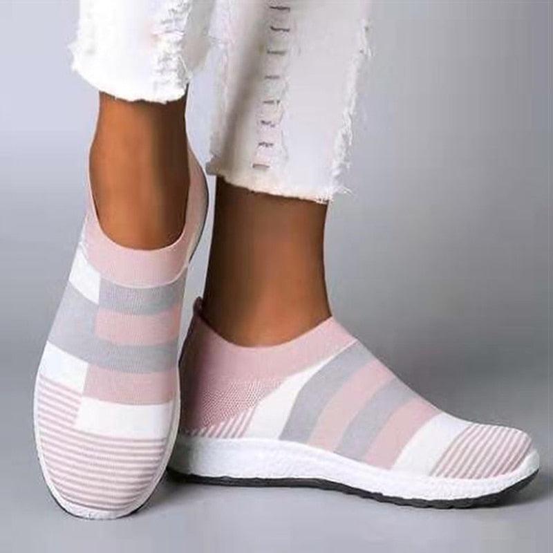 Pink and gray striped shoes worn with white pants on a gray background