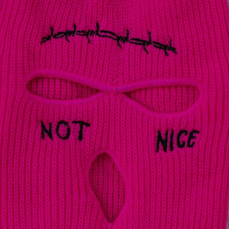 Pink knitted face mask with text 'NOT NICE' and a design resembling a face.