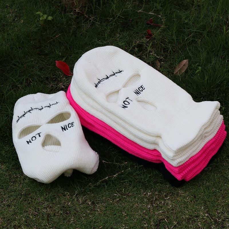 Stack of balaclava / Face masks with 'Not Nice' text on a grassy background