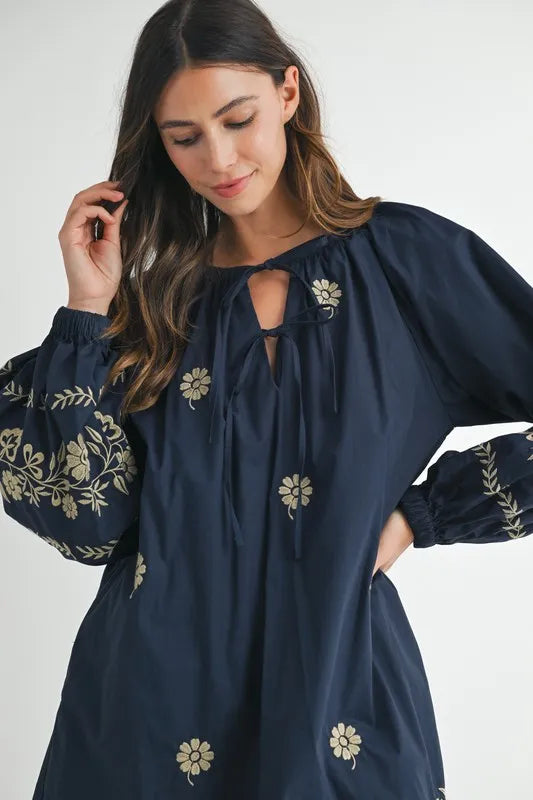 Woman wearing a navy blue dress with floral embroidery on a white background