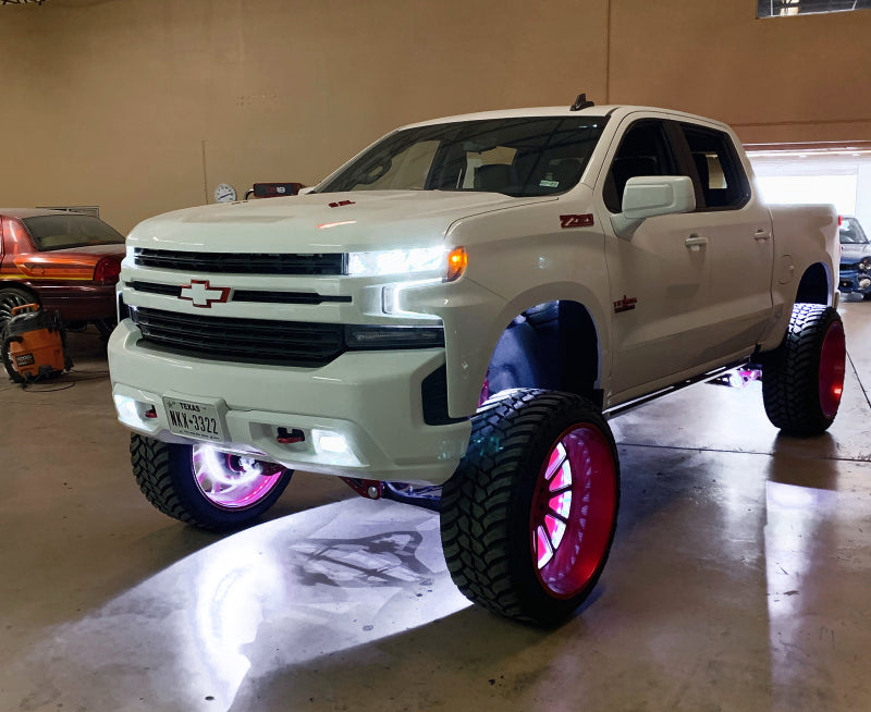 White pickup truck with large wheels and underbody lighting inside a garage.