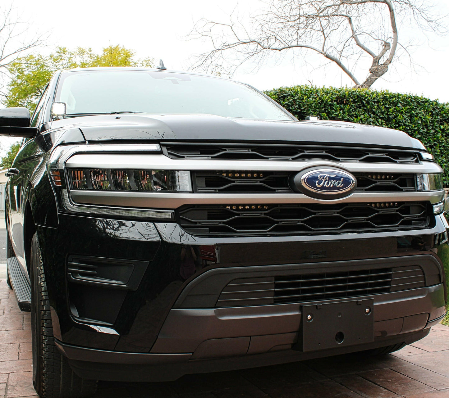 Front view of a black Ford SUV with  LED Light Bars parked outdoors with trees and greenery in the background.