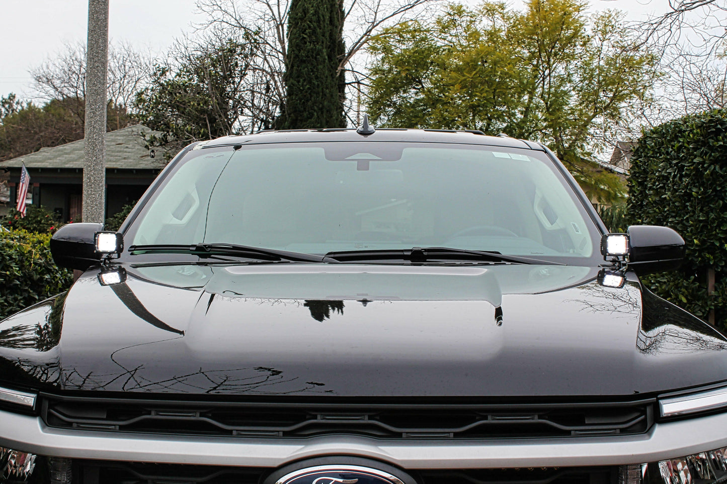 Front view of a black Ford truck with  a hood mounted light trees and a house in the background