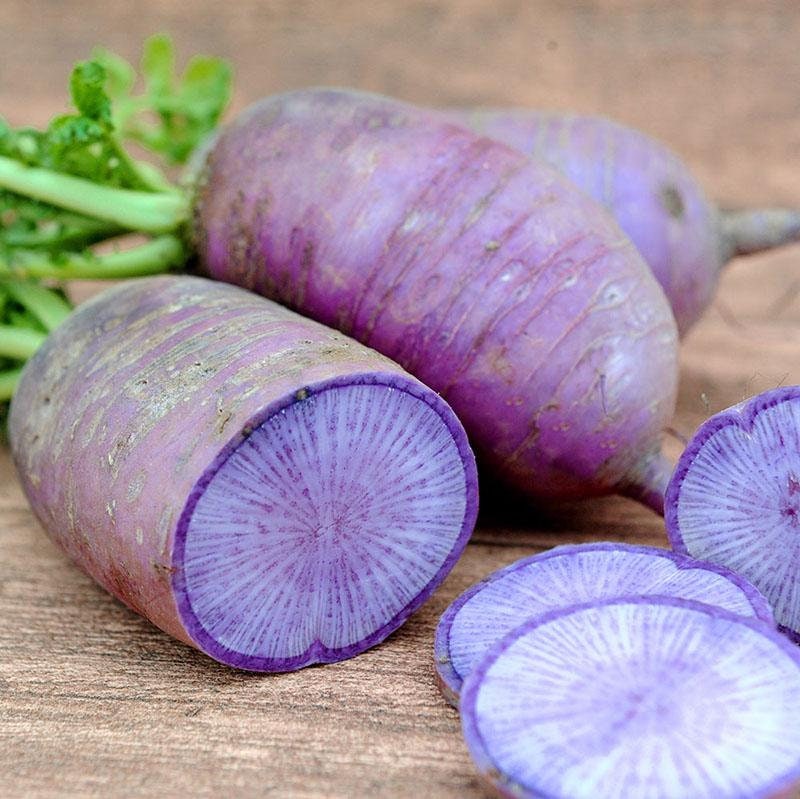 Purple daikon radishes on a wooden surface with some sliced.