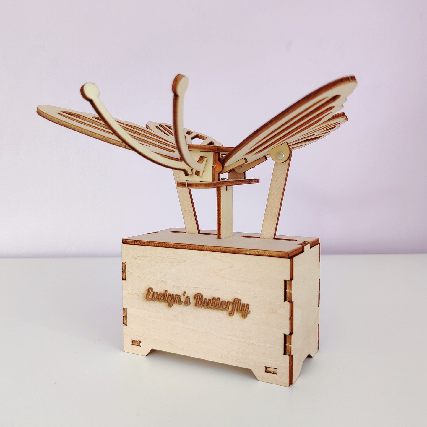 Wooden butterfly model on a white surface with a light purple background