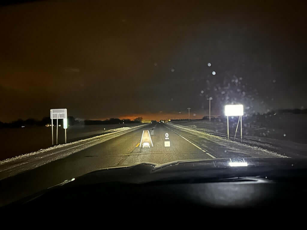 Nightscape of a snowy road with headlights on, viewed from inside a vehicle.