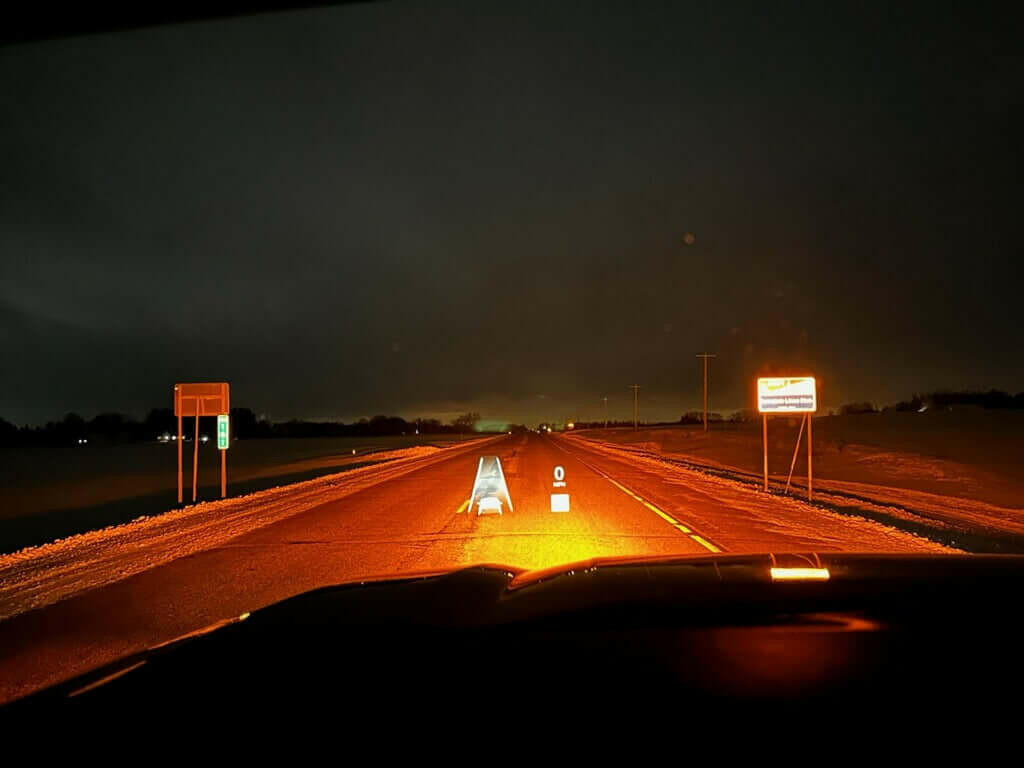 Nightime view from inside a car on a dark road with illuminated signs.