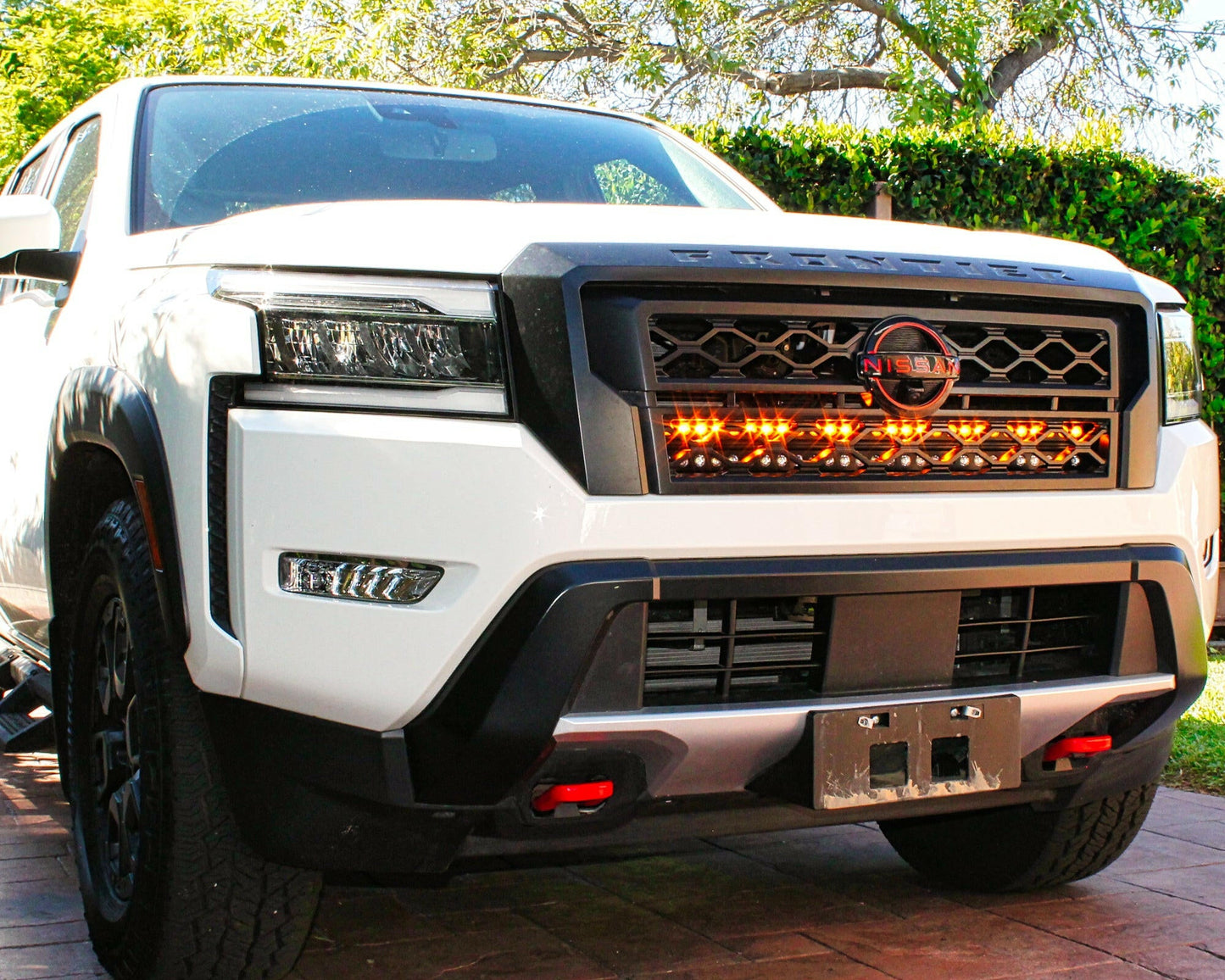 Front view of a white Nissan truck with illuminated grille in an outdoor setting