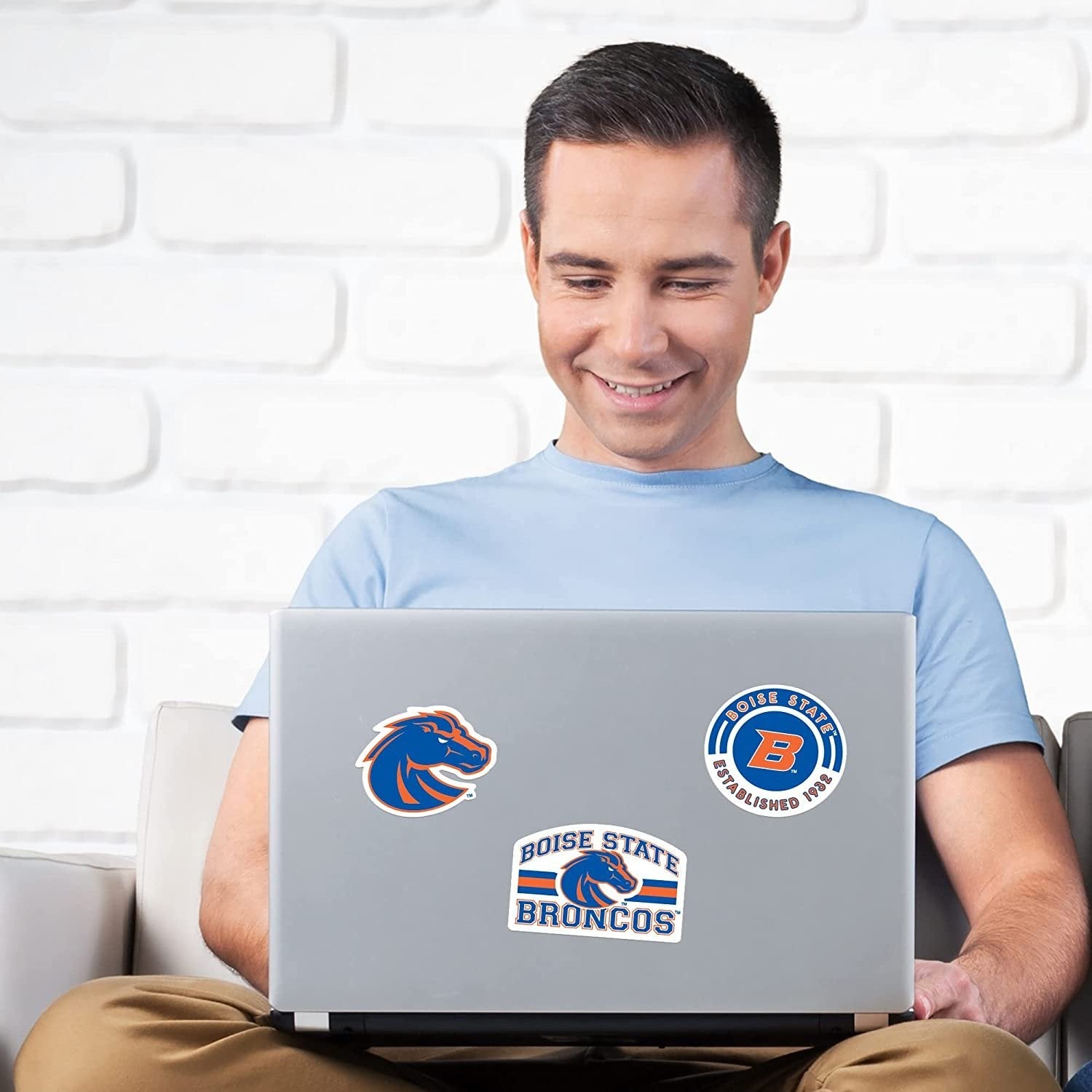 Man using a laptop with Sports stickers on a white brick wall background