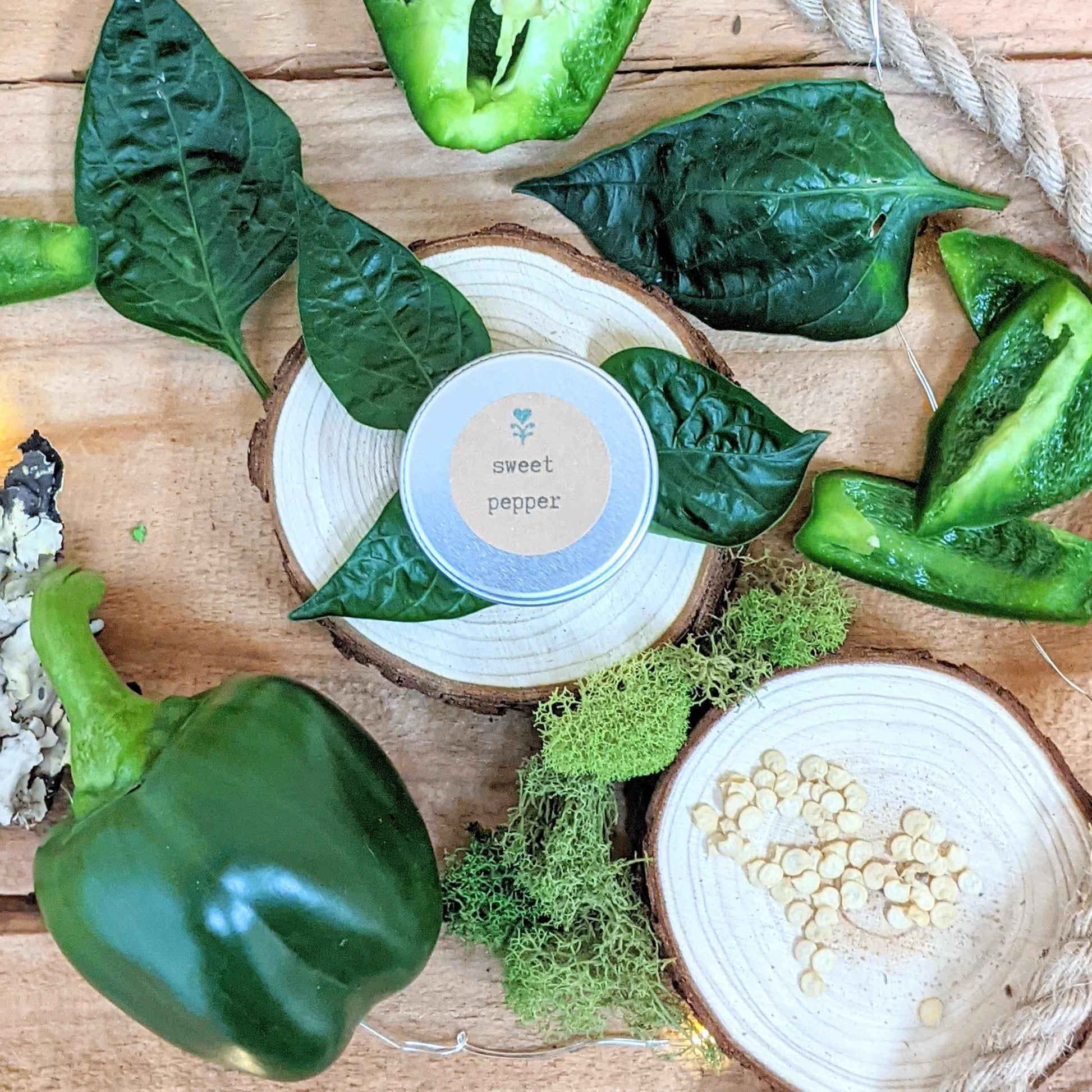Green peppers and leaves on a wooden surface with a 'sweet pepper' container.