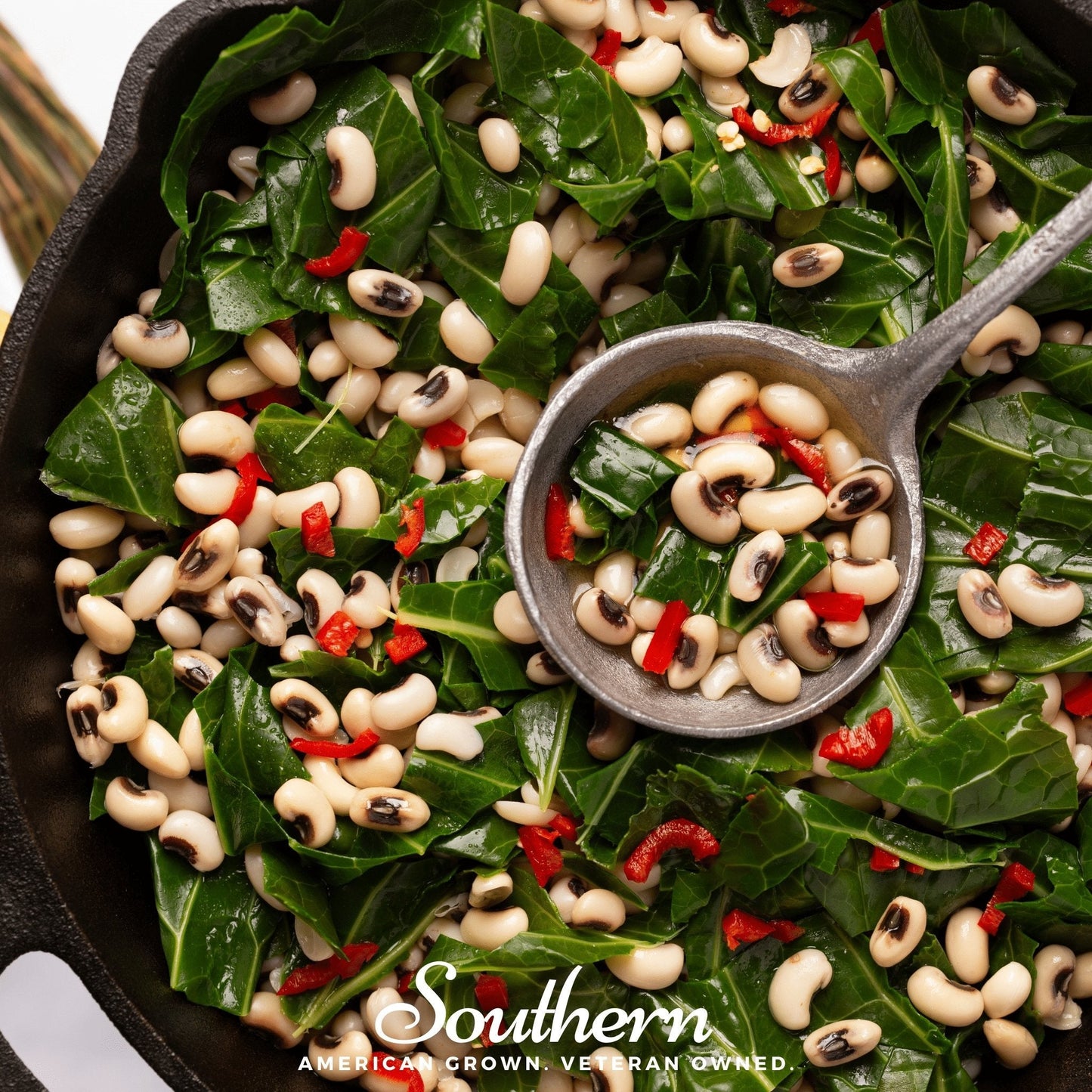 Black-eyed peas and greens in a cast iron skillet with a small bowl of peas.