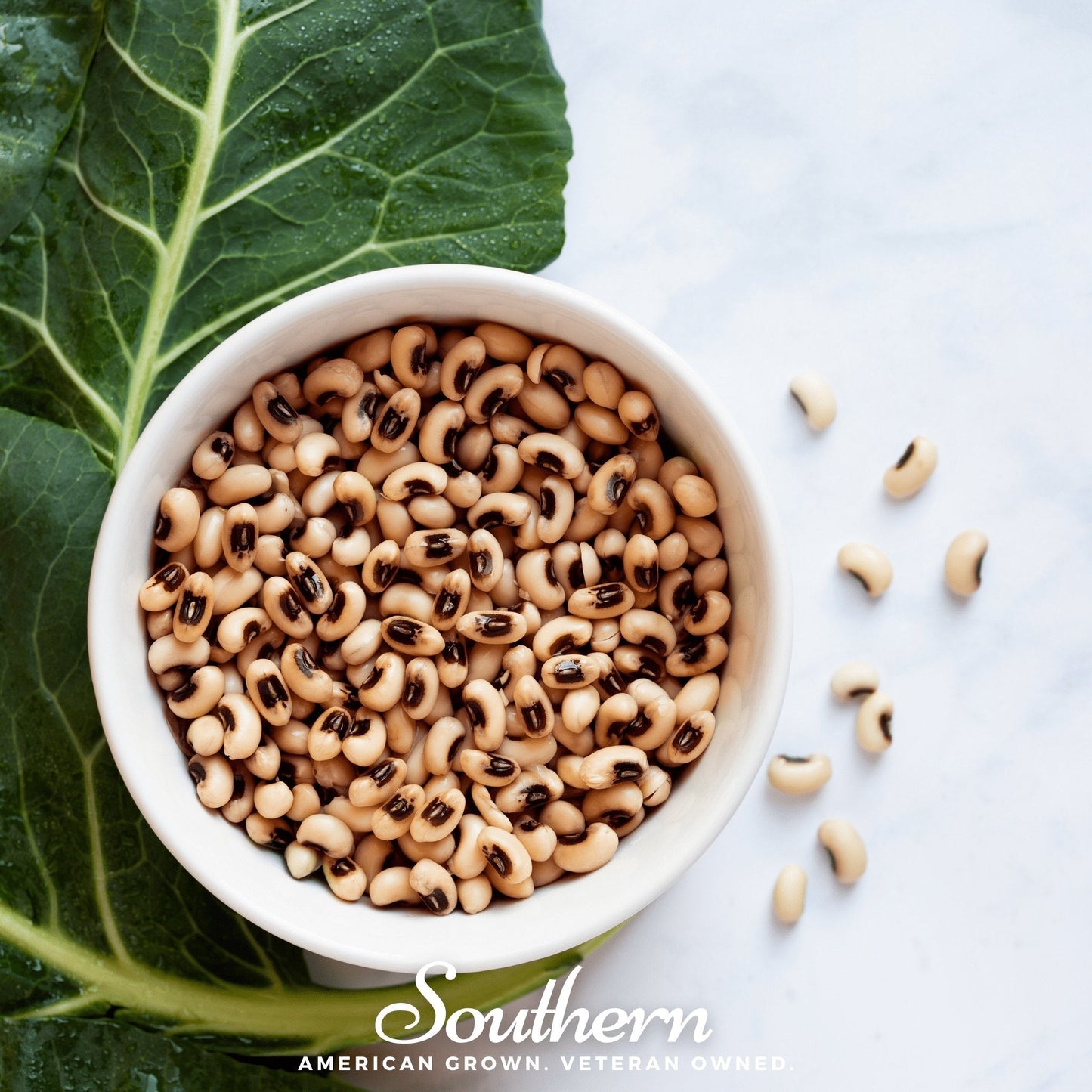 White bowl filled with black-eyed peas on a white background with collard greens.