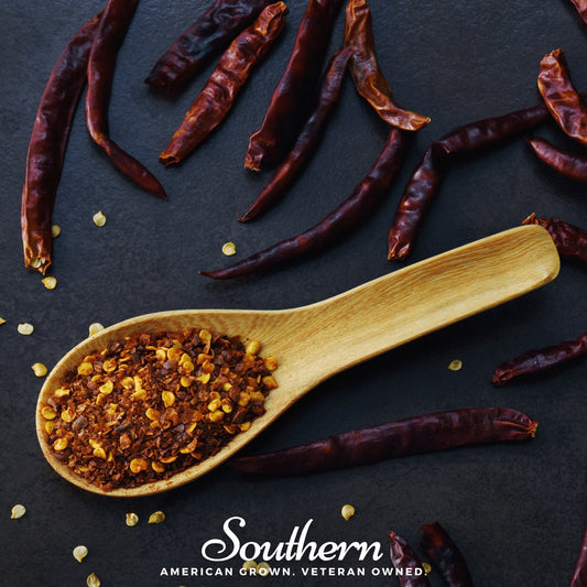Wooden spoon filled with ground pepper seeds on a dark surface with dried red peppers.