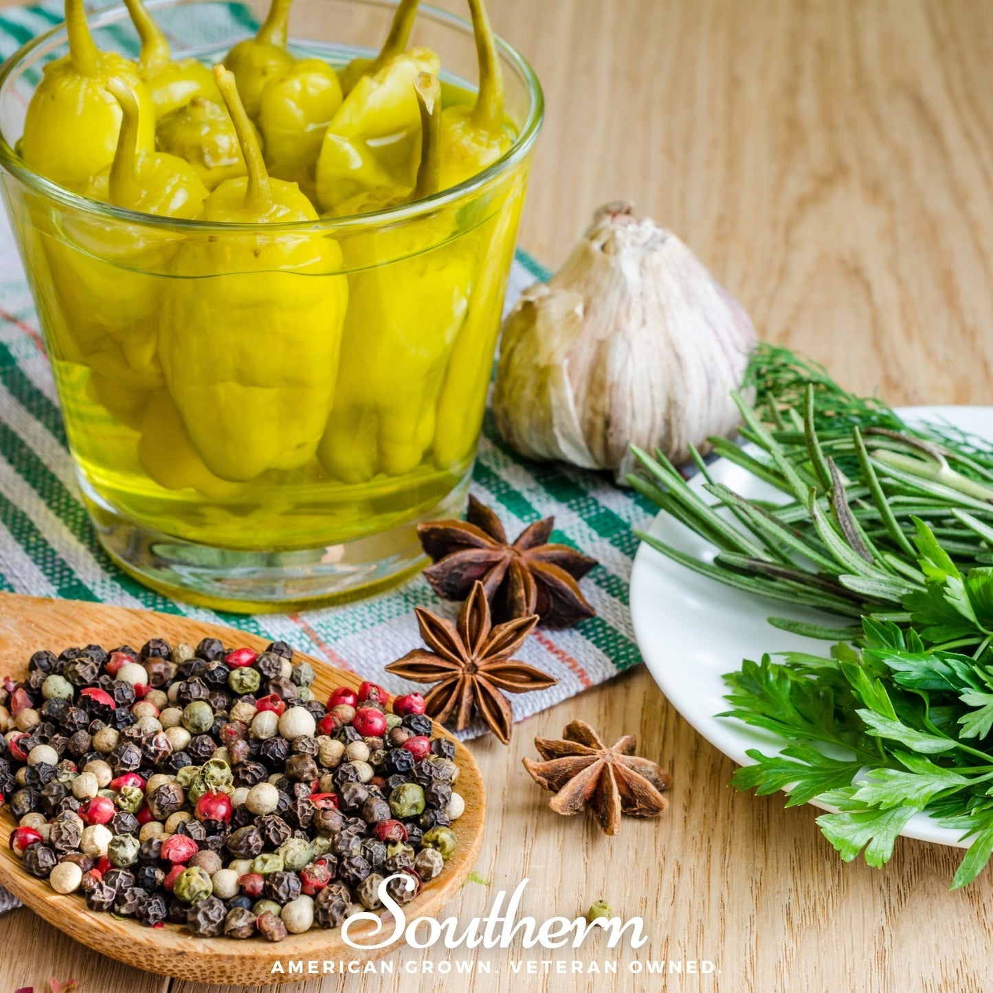 Glass jar of pickled peppers with herbs, spices, and garlic on a wooden surface.